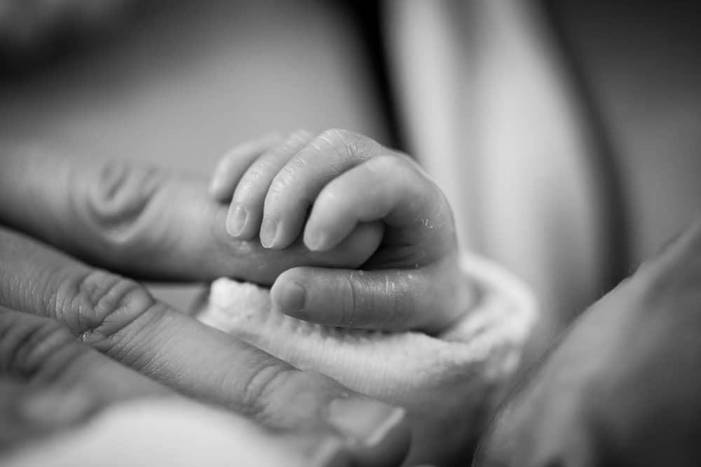 Newborn baby clutching Mom's finger